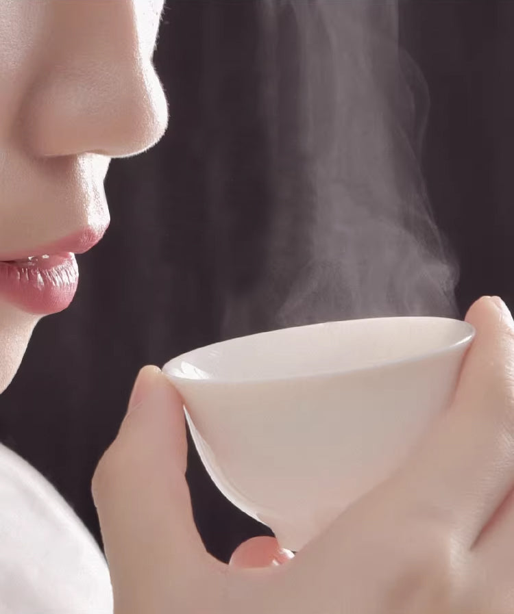 Person holding a steaming white ceramic tea cup near their face